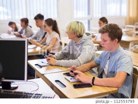 Modern teenagers sitting with mobile phones on lesson Modern teenagers sitting with mobile phones on lesson 112553793