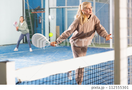 Woman serving ball while playing padel in court 112555301