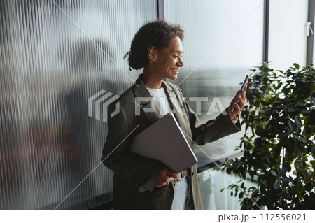 a woman is standing in front of a window holding a laptop and a cell phone 112556021