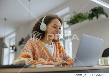 A woman at a table using a laptop computer with headphones on 112556069