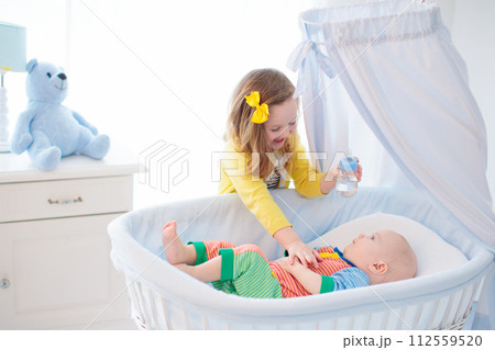 Little girl giving baby brother bottle with milk Little girl giving baby brother bottle with milk 112559520