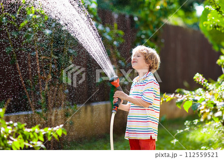 Boy watering flower in garden. Kid with water hose Boy watering flower in garden. Kid with water hose 112559521