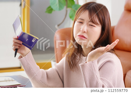 通帳を持って困った表情をしている女性 112559770