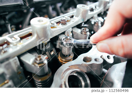 Car mechanic checking and adjusting valves of car engine 112560496