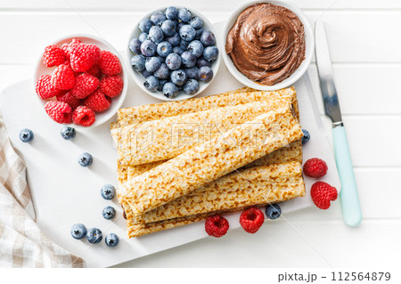 Freshly Made Crepes Topped With Raspberries and Blueberries on white table. Top view. Freshly Made Crepes Topped With Raspberries and Blueberries on white table. Top view. 112564879