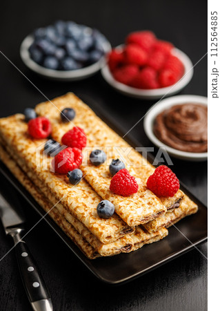 Delicate crepes stacked with blueberries and raspberries, served with a chocolate spread. Delicate crepes stacked with blueberries and raspberries, served with a chocolate spread. 112564885