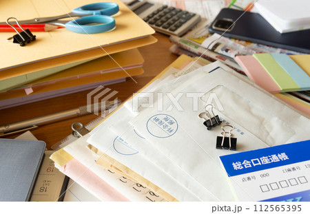 溜まった書類や郵便物で雑然とした机　散らかった机 112565395