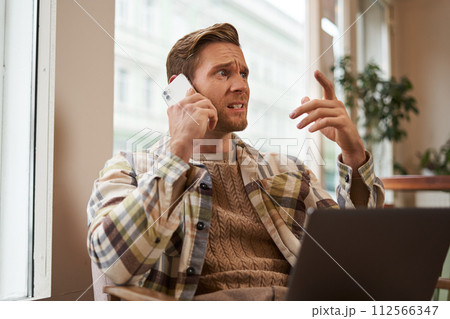 Image of man feeling stressed while talking over the phone. Businessman sitting in cafe with laptop, answering a call, hear bad news over the telephone Image of man feeling stressed while talking over the phone. Businessman sitting in cafe with laptop, answering a call, hear bad news over the telephone 112566347