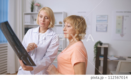 A concentrated traumatologist and a senior patient examine an X-ray image, discussing the diagnosis A concentrated traumatologist and a senior patient examine an X-ray image, discussing the diagnosis 112567014