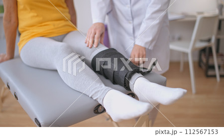 An orthopedist assesses a patient's leg in an orthopedic brace, aiding rehabilitation after a sprain injury 112567153