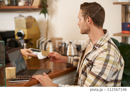 Portrait of freelancer, young man with laptop in coffee shop, paying for his order, pressing his credit card to the POS terminal, contactless payment concept 112567196