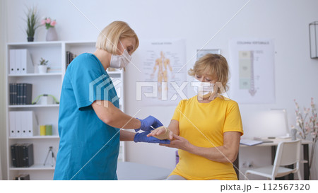 A nurse applies a medical band to a senior patient's injured hand, providing trauma treatment A nurse applies a medical band to a senior patient's injured hand, providing trauma treatment 112567320