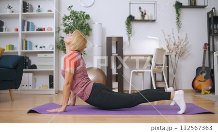 A middle-aged woman performs yoga and stretching exercises at home, leading a healthy lifestyle 112567363