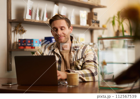 Portrait of handsome young digital nomad, man working in cafe on laptop, looking happy and pleased with his online project, sitting in co-working coffee shop Portrait of handsome young digital nomad, man working in cafe on laptop, looking happy and pleased with his online project, sitting in co-working coffee shop 112567539