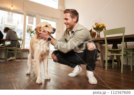 Close up portrait of happy dog owner, man with his pet giving a treat, spending time in animal-friendly cafe or co-working space 112567600