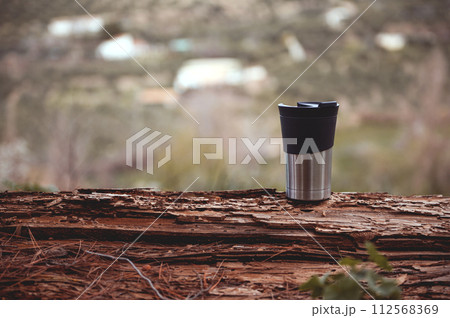 Horizontal shot of a travel mug on a log over blurred nature background with copy advertising space 112568369