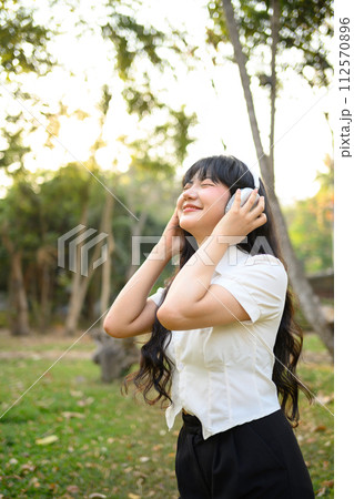 Attractive girl listening to favorite audio tracks with headphones in the park Attractive girl listening to favorite audio tracks with headphones in the park 112570896