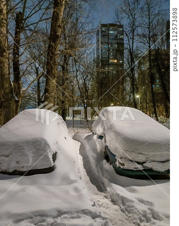 A narrow path in the snow between snow-covered cars on a winter evening in the city A narrow path in the snow between snow-covered cars on a winter evening in the city 112573898