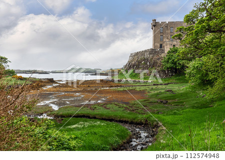 Historic Dunvegan Castle on Isle of Skye, surrounded by vibrant green flora under a dynamic sky Historic Dunvegan Castle on Isle of Skye, surrounded by vibrant green flora under a dynamic sky 112574948