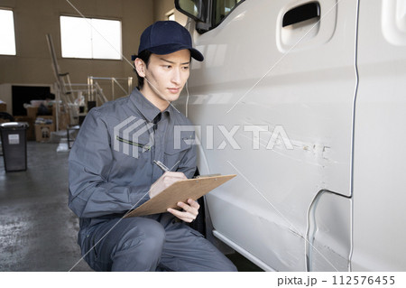 傷ついた車の修理の見積もりをする作業員 傷ついた車の修理の見積もりをする作業員 112576455