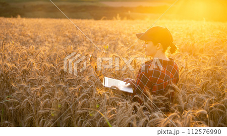 Woman farmer working with laptop on wheat field. Smart farming and digital agriculture Woman farmer working with laptop on wheat field. Smart farming and digital agriculture 112576990