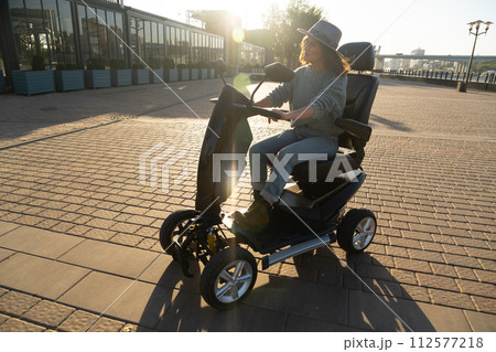 Woman tourist riding a four wheel mobility electric scooter on a city street 112577218