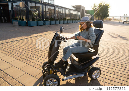 Woman tourist riding a four wheel mobility electric scooter on a city street 112577221