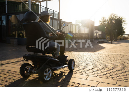 Woman tourist riding a four wheel mobility electric scooter on a city street 112577226