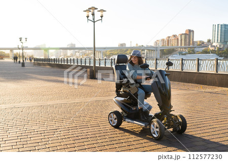 Woman tourist riding a four wheel mobility electric scooter on a city street 112577230