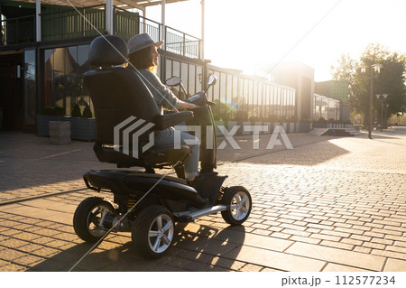 Woman tourist riding a four wheel mobility electric scooter on a city street 112577234