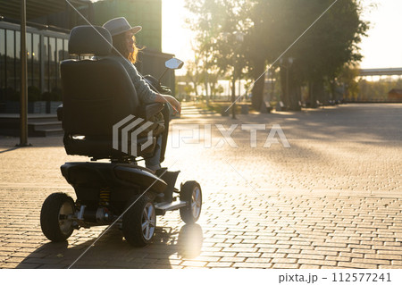 Woman tourist riding a four wheel mobility electric scooter on a city street 112577241