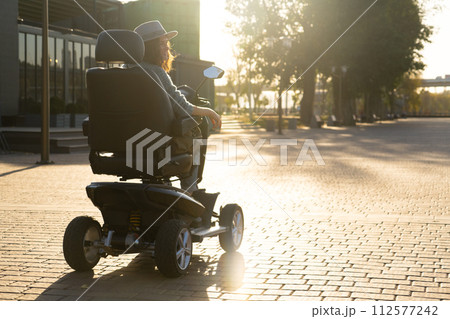 Woman tourist riding a four wheel mobility electric scooter on a city street 112577242