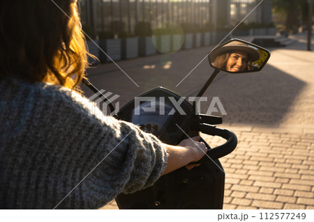 Woman tourist on a four wheel mobility electric scooter on a city street. The woman's face is visible in the rearview mirror.. 112577249