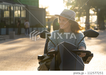 Woman tourist riding a four wheel mobility electric scooter on a city street 112577251