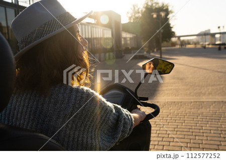 Woman tourist on a four wheel mobility electric scooter on a city street. The woman's face is visible in the rearview mirror.. 112577252