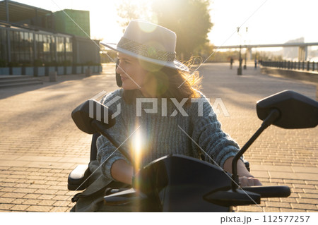 Woman tourist riding a four wheel mobility electric scooter on a city street 112577257