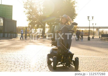 Woman tourist riding a four wheel mobility electric scooter on a city street 112577260