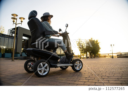 Woman tourist riding a four wheel mobility electric scooter on a city street 112577265