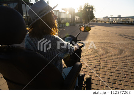 Woman tourist on a four wheel mobility electric scooter on a city street. The woman's face is visible in the rearview mirror.. 112577268
