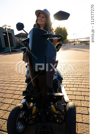 Woman tourist riding a four wheel mobility electric scooter on a city street 112577270