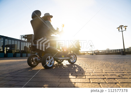 Woman tourist riding a four wheel mobility electric scooter on a city street 112577378