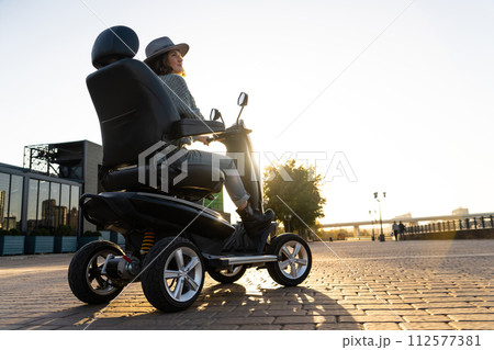 Woman tourist riding a four wheel mobility electric scooter on a city street 112577381