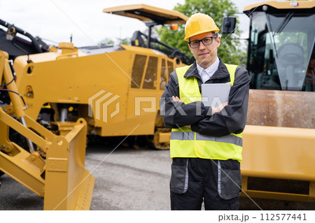 Engineer with digital tablet next to road construction machine 112577441