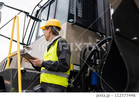 Engineer with tablet computer stands on the stairs to the cab of a truck.. 112577446