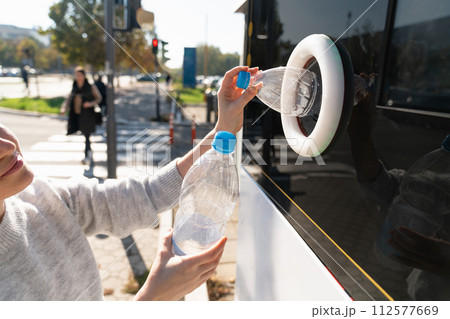 Woman uses a self service machine to receive used plastic bottles and cans on a city street.. 112577669