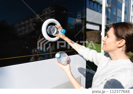 Woman uses a self service machine to receive used plastic bottles and cans on a city street.. 112577688