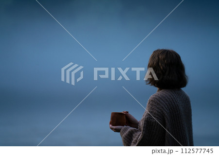 A woman in a sweater on the bank of a foggy river in the evening.. 112577745