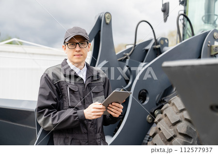 Serviceman with digital tablet on a background of the tractor Serviceman with digital tablet on a background of the tractor 112577937