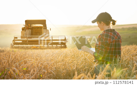 Woman farmer with digital tablet on a background of harvester. Smart farming concept 112578141