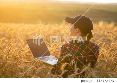 Woman farmer working with laptop on wheat field. 112578173